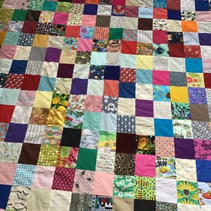 Könnte beinhalten: Ein Patchwork-Quilt aus zahlreichen Stoffquadraten in verschiedenen Farben und Mustern. Der Quilt zeigt Quadrate in Unifarben, Blumenmustern, Tiermustern und anderen Designs, wodurch ein lebendiges und strukturiertes Textil entsteht.
