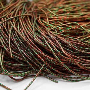 May include: A close-up of a spool of red and green metallic thread. The thread is shiny and has a slight sparkle to it.