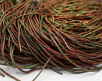 May include: A close-up of a spool of red and green metallic thread. The thread is shiny and has a slight sparkle to it.