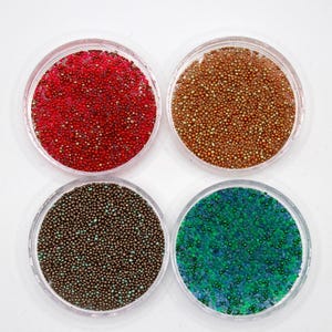 May include: Four small containers filled with colourful, iridescent microbeads. The beads are in shades of red, gold, brown, and green.