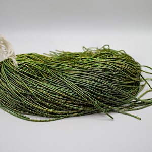 May include: A bundle of metallic green cord, tightly wound and tied with a white string. The cord has a shimmering, iridescent quality, with hints of gold. The overall appearance suggests a craft or jewelry-making material.