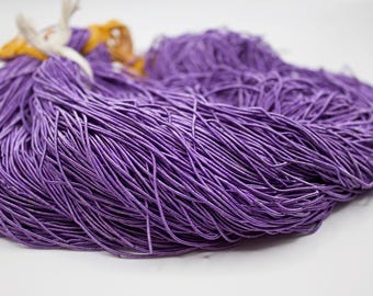 May include: A large bundle of vibrant purple cord, tightly packed together. The cords are thin and appear to be made of a flexible material. A small amount of yellow and white material is visible at the top, possibly used for tying the bundle.