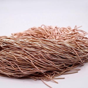 May include: A bundle of copper-colored wire, tightly wound and tied with a natural fiber string. The wire has a metallic sheen and is arranged in a dense, textured pile. The background is plain white.