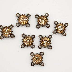 May include: Seven bronze metal embellishments, each featuring a central amber-coloured rhinestone. The embellishments have a cross-shaped design with four loops and a central, round rhinestone.