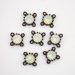 May include: Seven antique bronze-toned metal embellishments with a central, round, opalescent crystal. Each piece has a cross-shaped design with four decorative loops around the crystal. The crystals have a subtle, iridescent sheen.