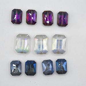 May include: Twelve rectangular glass beads in three colors: purple, clear with iridescent shimmer, and blue. The beads are arranged in three rows of four.