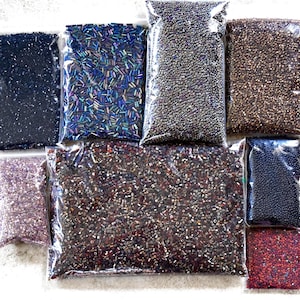 Puede incluir: Surtido de cuentas de semillas en varios colores y tamaños, incluyendo negro, plateado, marrón, morado, rojo y azul iridiscente. Las cuentas están empaquetadas en bolsas de plástico transparentes.