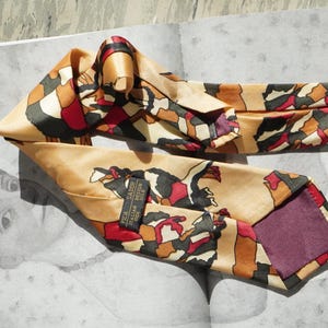 Könnte beinhalten: Eine Krawatte mit beigefarbener Basis und einem abstrakten Muster aus schwarzen, roten und braunen Formen. Die Krawatte enthält ein schwarzes Etikett mit weißem Text PICA SADOR ITALIAN DESIGN SILK und ein violettes Innenfutter am breiten Ende.