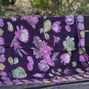 Peut inclure: Un foulard carré de couleur violet foncé orné d'un motif répétitif représentant divers choux et légumes dans des tons magenta, vert clair et crème. Le foulard présente une fine bordure de couleur claire et une signature visible dans le coin.