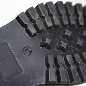 May include: A black rubber shoe sole featuring a deep, lugged tread pattern for traction. The sole includes a rectangular recessed area and a circular stamp displaying the number 37, indicating the size of the footwear in a standard format.