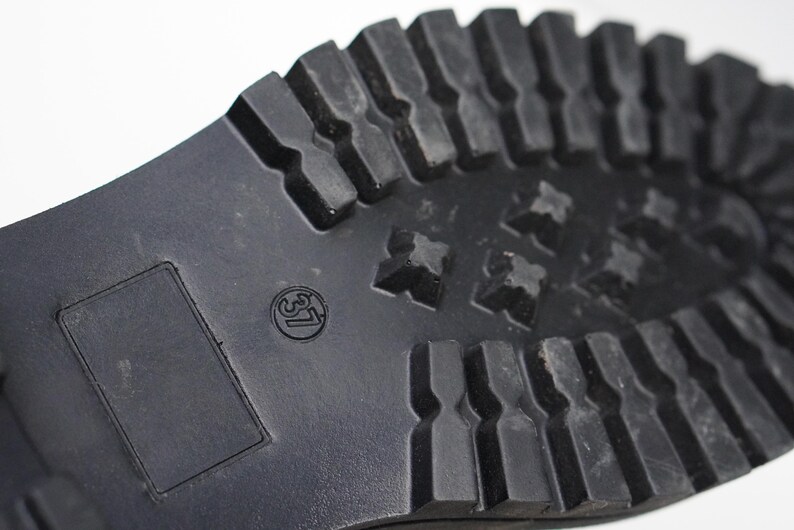 May include: A black rubber shoe sole featuring a deep, lugged tread pattern for traction. The sole includes a rectangular recessed area and a circular stamp displaying the number 37, indicating the size of the footwear in a standard format.