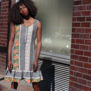 Peut inclure: Robe sans manches en patchwork avec des motifs floraux et géométriques. La robe présente un ourlet à volants et un devant boutonné. La palette de couleurs comprend l'orange, le vert, le noir, le blanc et le gris. La robe est en tissu léger.
