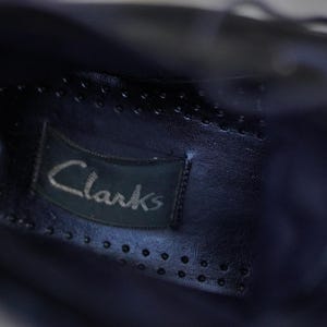 Op de afbeelding: Close-up van de binnenkant van een donkerblauwe leren schoen. Het Clarks-merklabel is zichtbaar, op de binnenzool genaaid. De binnenzool heeft kleine, gelijkmatig verdeelde perforaties.