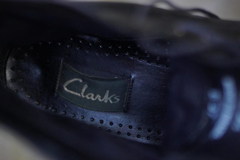 Op de afbeelding: Close-up van de binnenkant van een donkerblauwe leren schoen. Het Clarks-merklabel is zichtbaar, op de binnenzool genaaid. De binnenzool heeft kleine, gelijkmatig verdeelde perforaties.