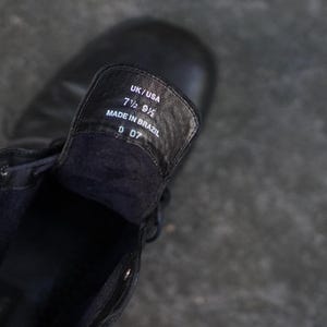 Op de afbeelding: Zwarte leren laars met het binnenlabel zichtbaar. Het label luidt "UK/USA 7 1/2 9 1/2 MADE IN BRAZIL D 07". De laars is geregen en lijkt nieuw.