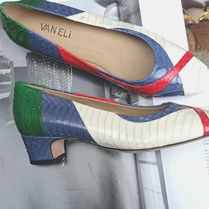 May include: A pair of VAN ELI low-heeled pumps featuring a multi-coloured snakeskin-textured pattern in green, blue, red, and cream. The shoes have a pointed toe, a low block heel, and a tan interior lining with the brand name printed in black.