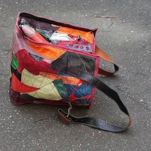 Può includere: Borsa in pelle patchwork multicolore con tracolla nera. La borsa presenta colori come rosso, arancione, verde e blu. La borsa è aperta, rivelando l'interno.
