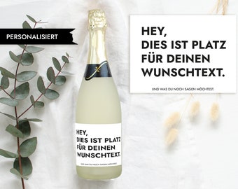 Può includere: Una bottiglia di vino spumante in vetro trasparente con un'etichetta bianca che dice "HEY, DIES IST PLATZ FÜR DEINEN WUNSCHTEXT. UND WAS DU NOCH SAGEN MÖCHTEST."