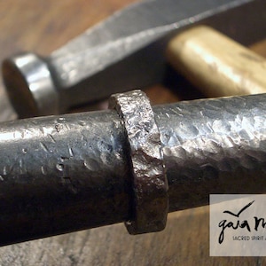 Könnte beinhalten: Nahaufnahme eines silbernen Metallrings mit gehämmerter Textur. Der Ring ist aus dickem Metall gefertigt und hat ein raues, unfertiges Aussehen. Der Ring ist Teil eines größeren Metallstücks, das ebenfalls gehämmert ist und eine raue Textur aufweist.