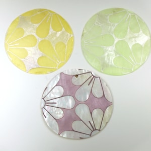 May include: Three round, decorative, mother-of-pearl ornaments with floral designs. The ornaments are yellow, green, and purple.