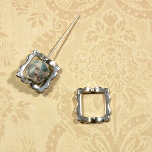 May include: Two silver metal picture frames with ornate edges. The larger frame has a blue and green patterned bead inside.