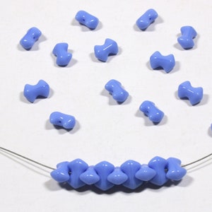 May include: A close-up of a string of light blue glass beads with a pointed, teardrop shape. The beads are strung on a silver wire and there are several loose beads scattered around the wire.
