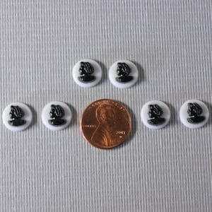 May include: Six black and white glass buttons with a silhouette of a woman's head in profile. The buttons are about the size of a US penny.