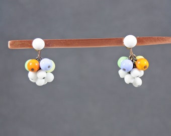 May include: A pair of dangle earrings with a cluster of white, orange, light blue, and green beads. The earrings are hanging from a copper stand.