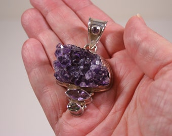 May include: A silver pendant featuring a large amethyst cluster with smaller amethyst and green stones.