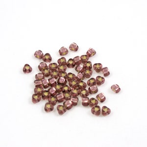 May include: A pile of small, square, translucent beads in a light purple color. The beads have a slight shimmer to them.