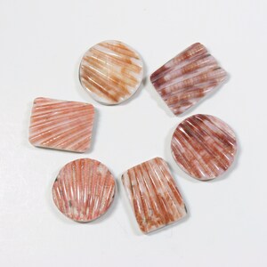 May include: Six shell cabochons in various shapes and sizes. The cabochons are a mix of white and pink with brown striations.