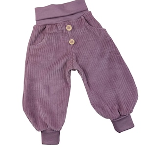 Könnte beinhalten: Lavendelfarbene Cordhose mit breitem Bund und zwei Holzknöpfen. Die Hose hat zwei Vordertaschen und elastische Bündchen. Der Stoff hat eine vertikale Rippstruktur.