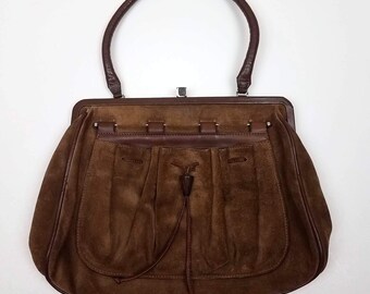 May include: A brown suede handbag with a top handle and a drawstring closure. The bag has a flap with a metal clasp.