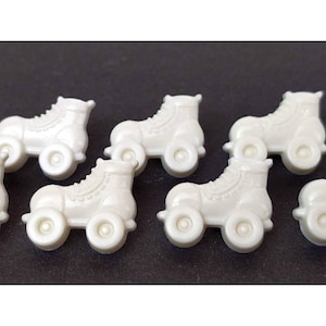 May include: Six white plastic roller skate buttons. The buttons are about 1 inch in diameter and have a raised design.