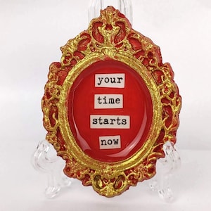 May include: A red and gold oval frame with the words "your time starts now" in white lettering.