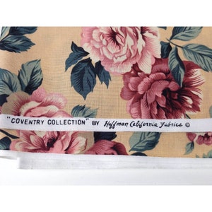 May include: A beige fabric with a floral print featuring pink and red roses and green leaves. The fabric has a white label that reads "COVENTRY COLLECTION" BY Hoffman California Fabrics &copy;