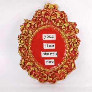 May include: A red and gold ornate frame with the words "your time starts now" in white lettering.
