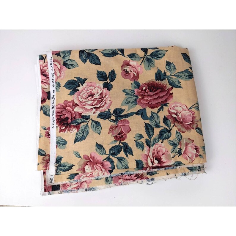 May include: A beige fabric with a floral print featuring pink roses and green leaves. The fabric is labeled "COUNTRY COLLECTION by Hycraft  Elegant Fabrics Co."