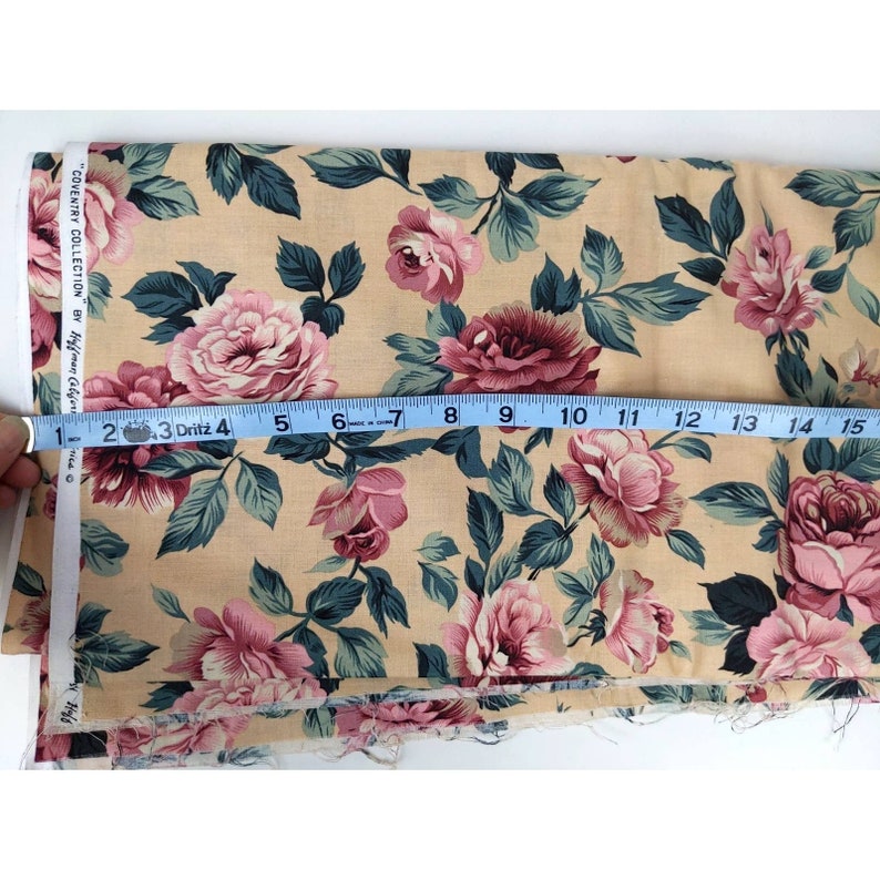 May include: Beige fabric with a floral print featuring pink and burgundy roses with green leaves. The fabric is measured with a tape measure, showing 15 inches.