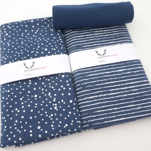 Può includere: Rotoli di tessuto jersey blu navy. Uno presenta pois bianchi, l'altro righe orizzontali bianche. Un rotolo di tessuto blu navy tinta unita è sopra. Ogni rotolo ha una fascia bianca con il testo "stoffrevier Jersey".