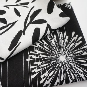 Könnte beinhalten: Nahaufnahme von gefaltetem Stoff mit schwarz-weißen Mustern. Ein Abschnitt zeigt schwarze, blattartige Pinselstriche auf weißem Hintergrund. Ein anderer Abschnitt hat ein weißes Radialdesign auf schwarzem Hintergrund. Geeignet für Heimdekoration oder Mode.