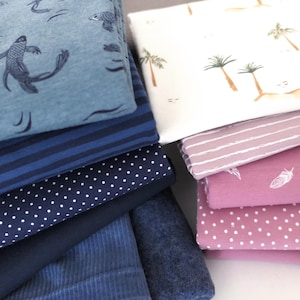 Op de afbeelding: Een stapel verschillende stoffen met patronen. De stoffen omvatten blauw met vis- en schildpadontwerpen, marineblauw met witte stippen en roze met witte veren. Andere stoffen hebben strepen en palmbomenpatronen.