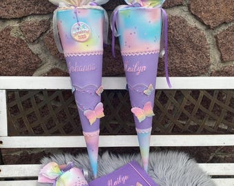 May include: Three purple and pastel-colored school cones with butterfly accents and personalized names. A matching purple book with butterfly embellishments and the name "Marilyn" is also present. The cones are decorated with lace and ribbons.