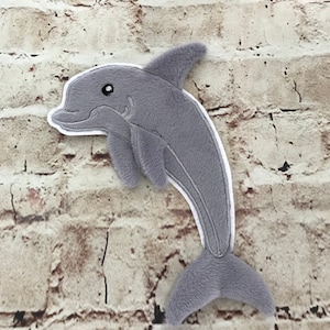 Könnte beinhalten: Ein grauer Plüschdelfin mit weißem Umriss, mit detailliertem Auge und Flossen. Der Delfin besteht aus weichem, strukturiertem Material und ist so gestaltet, dass er einem echten Delfin ähnelt. Das Plüschtier ist ein süßes und kuscheliges Produkt.