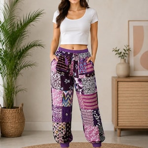 May include: A white short-sleeved scoop neck crop top paired with purple patchwork joggers featuring various floral, geometric, and abstract patterns in shades of violet, lavender, and white, finished with a purple elastic waistband and cuffs.