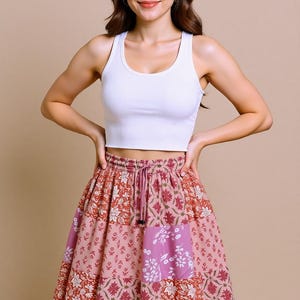 Op de afbeelding: Een witte geribbelde tanktop gecombineerd met een kleurrijke, bedrukte rok. De rok heeft een patchwork ontwerp met bloemen- en geometrische patronen in roze, rode en paarse tinten. De rok heeft een taille met trekkoord.