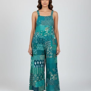 May include: A teal patchwork jumpsuit with wide legs and square neckline. The jumpsuit features various patterned fabric squares in shades of teal, green, and white. The straps are secured with buttons.