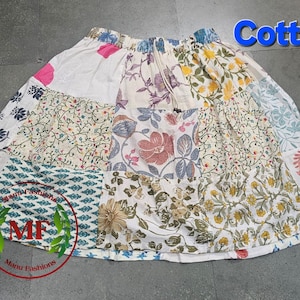 Peut inclure: Jupe en coton patchwork avec divers motifs floraux et botaniques en blanc, rose, bleu, jaune et vert. La jupe a une taille élastique et un cordon de serrage. Le mot "Cotton" est affiché en lettres bleues.
