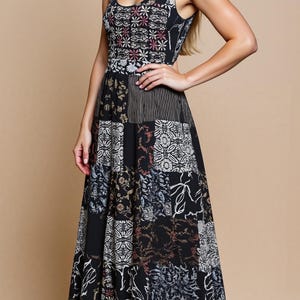 Op de afbeelding: Een mouwloze maxi-jurk met een patchwork-ontwerp. De jurk heeft een ronde hals en een getailleerd lijfje. De rok is een patchwork van verschillende patronen in zwart, wit en bruin. Het model draagt zwarte hakken.