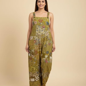 May include: Olive green jumpsuit with a patchwork design featuring floral and geometric patterns. The jumpsuit has wide legs, square neckline, and adjustable straps. The fabric appears to be lightweight and suitable for warm weather.